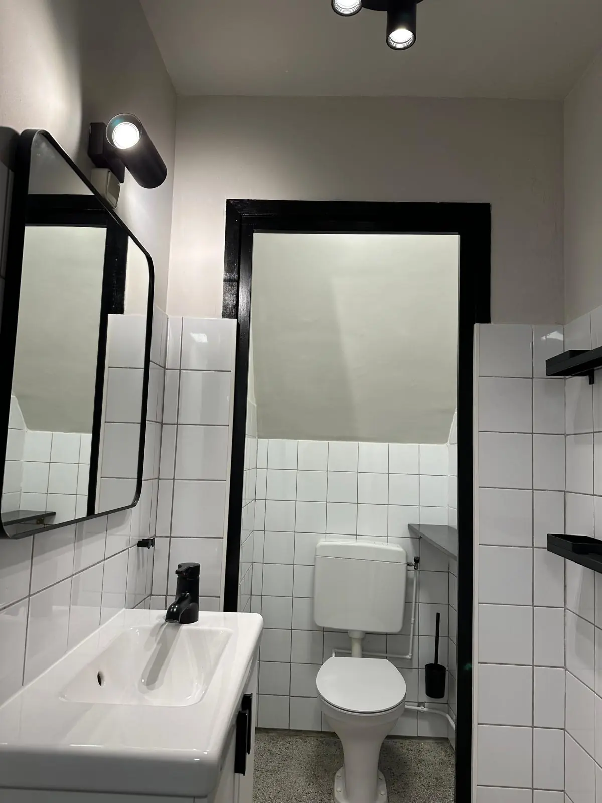 Modern, compact bathroom on Herengracht with white tiles, a toilet, sink, and minimalist black fixtures.