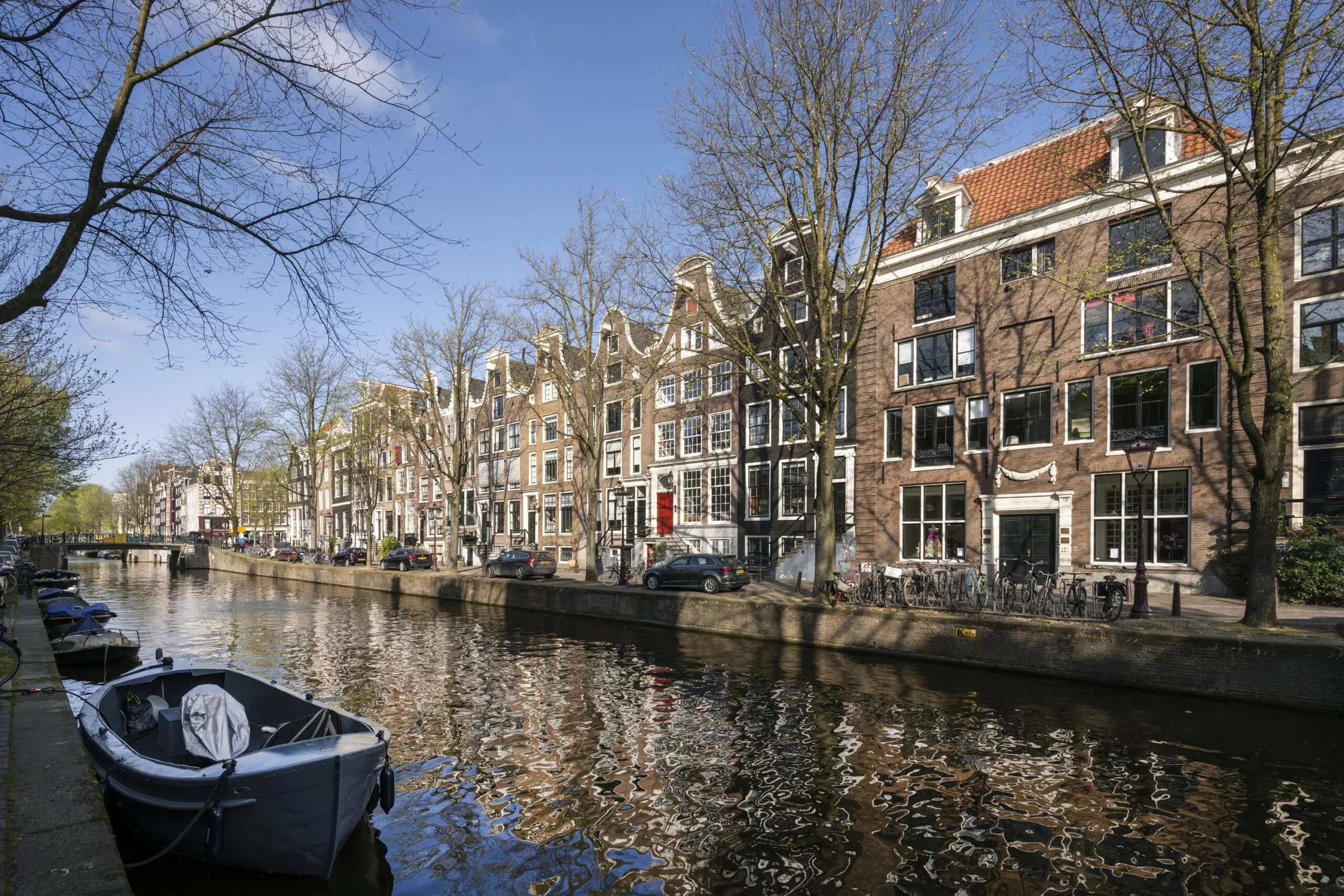 View of historic canal houses along Leidsegracht in Amsterdam with boats moored in the foreground.