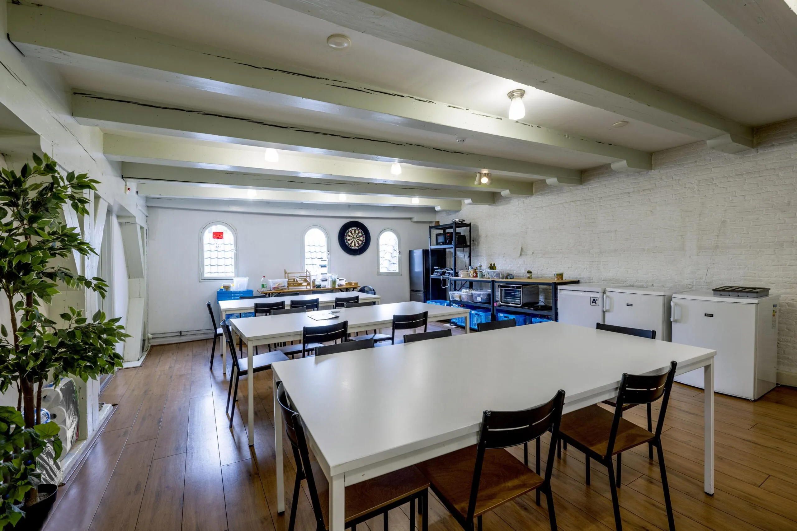 Bright communal kitchen and dining area on Leidsegracht with white tables, wooden floor, and cooking appliances.