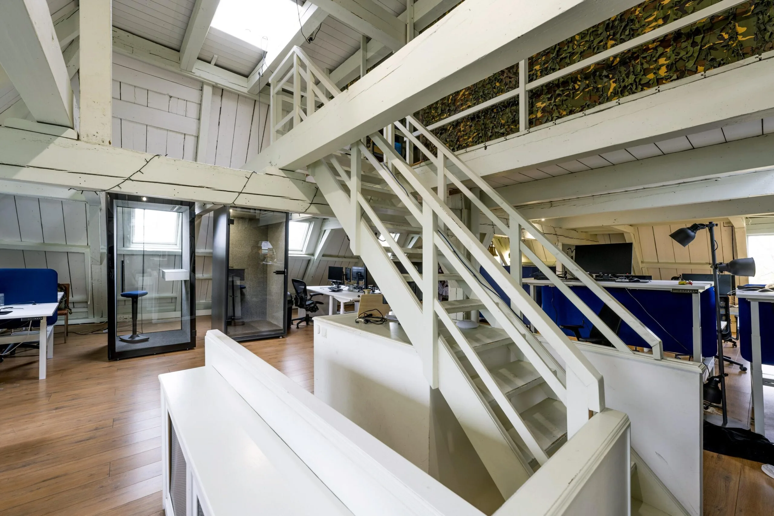 Modern attic office space on Leidsegracht with wooden beams, workstations, phone booths, and a white staircase.