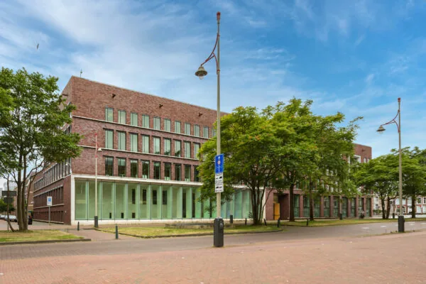 Modern brick office building on Carel van Bylandtlaan surrounded by trees under a clear blue sky.