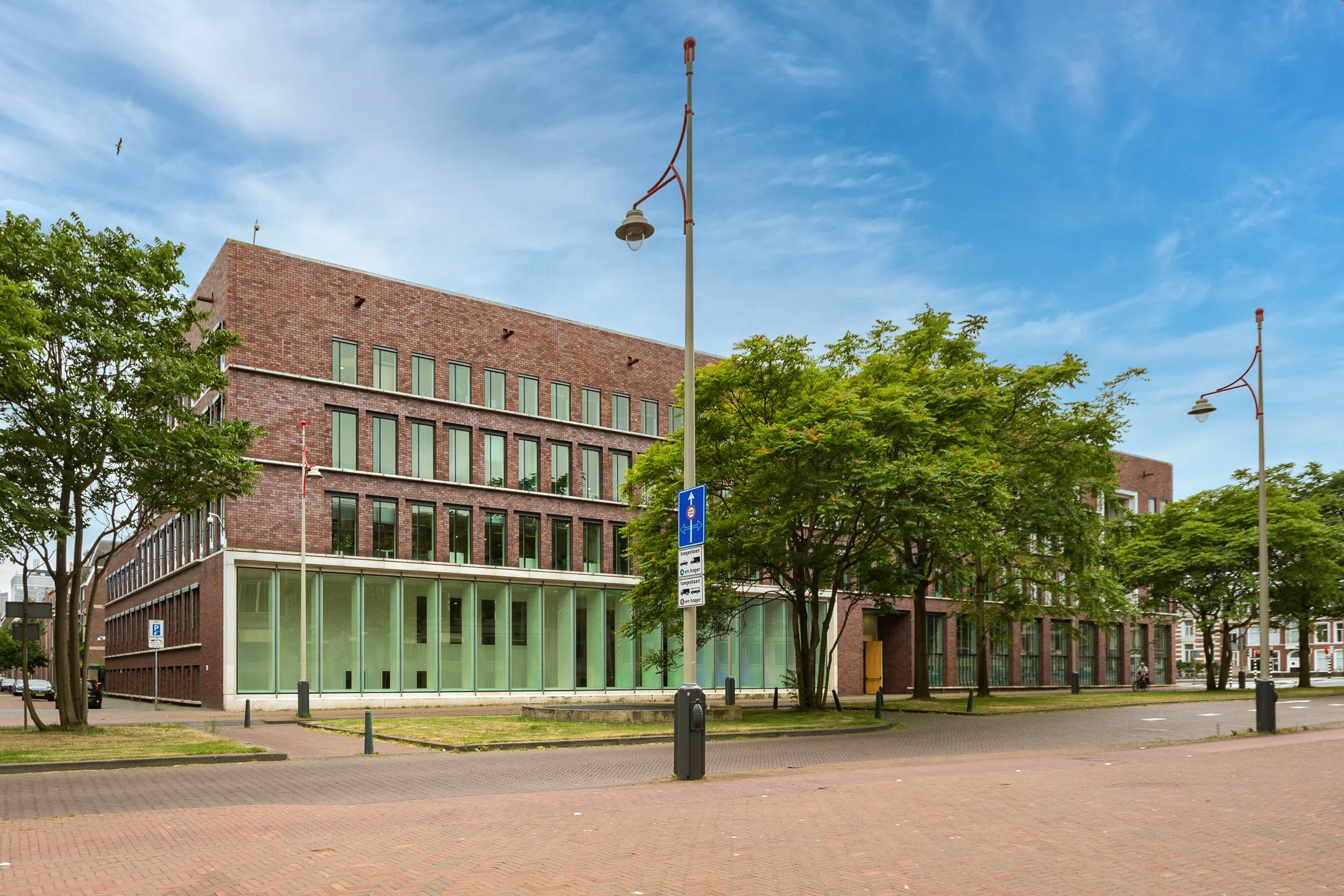 Modern brick office building on Carel van Bylandtlaan surrounded by trees under a clear blue sky.