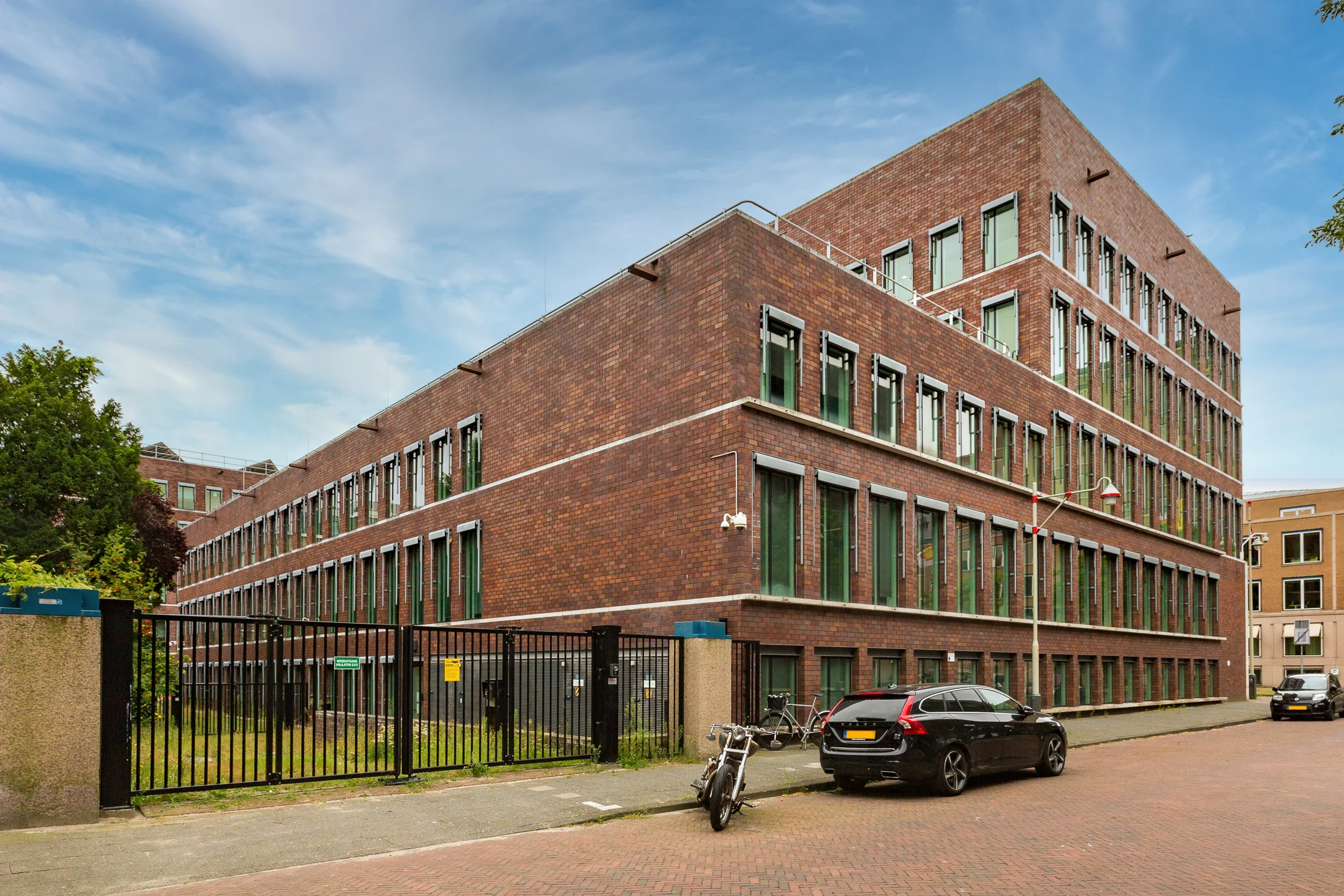Modern brick office building on Carel van Bylandtlaan with parked cars and bicycles in front.