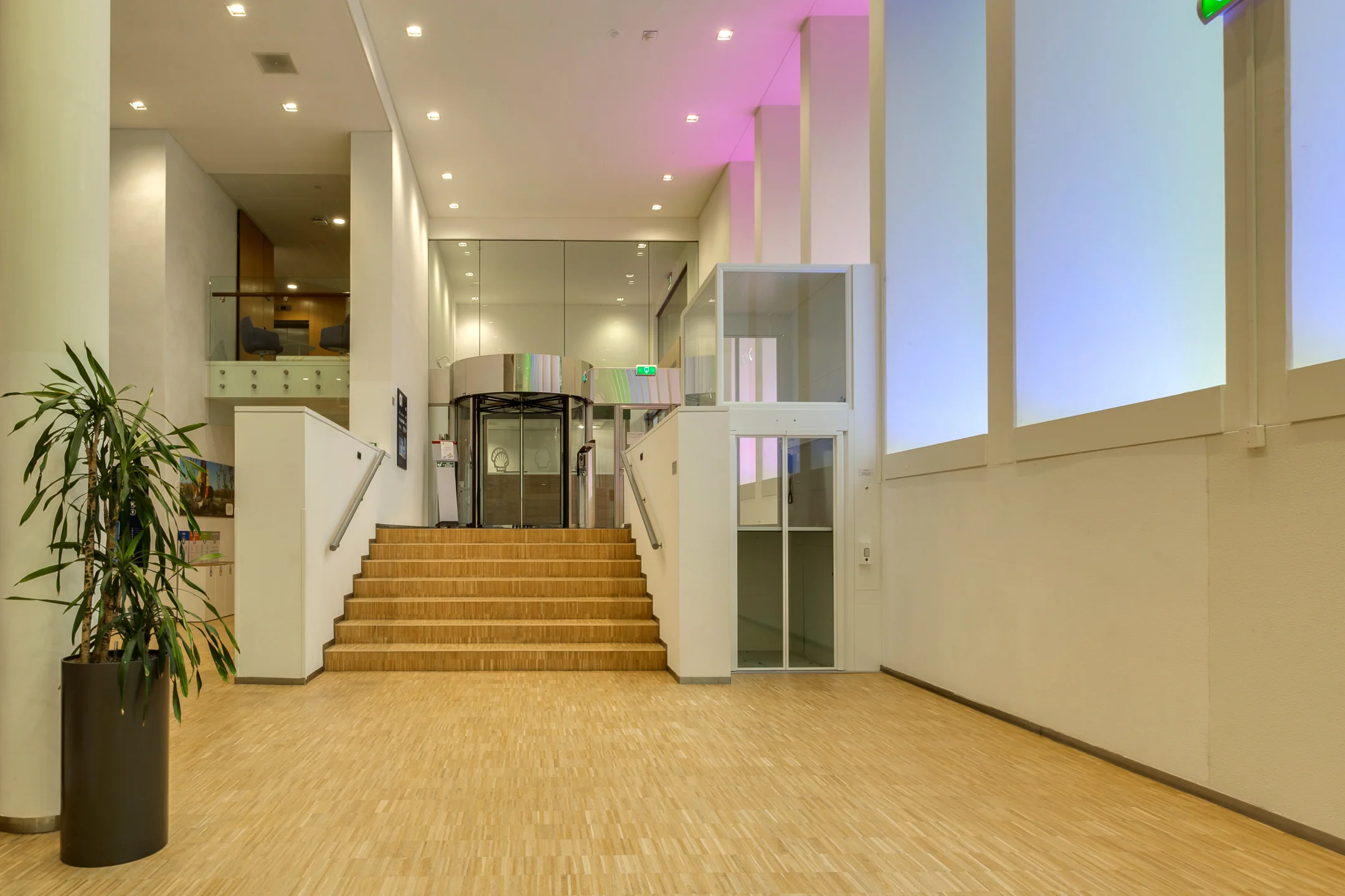 Modern lobby interior of an office building at Carel van Bylandtlaan with wooden flooring, a staircase, and a glass revolving door.