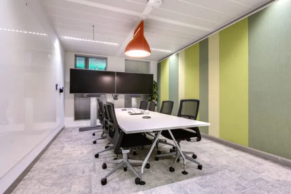 Modern conference room at Carel van Bylandtlaan with a large table, office chairs, dual screens, and striped green wall panels.