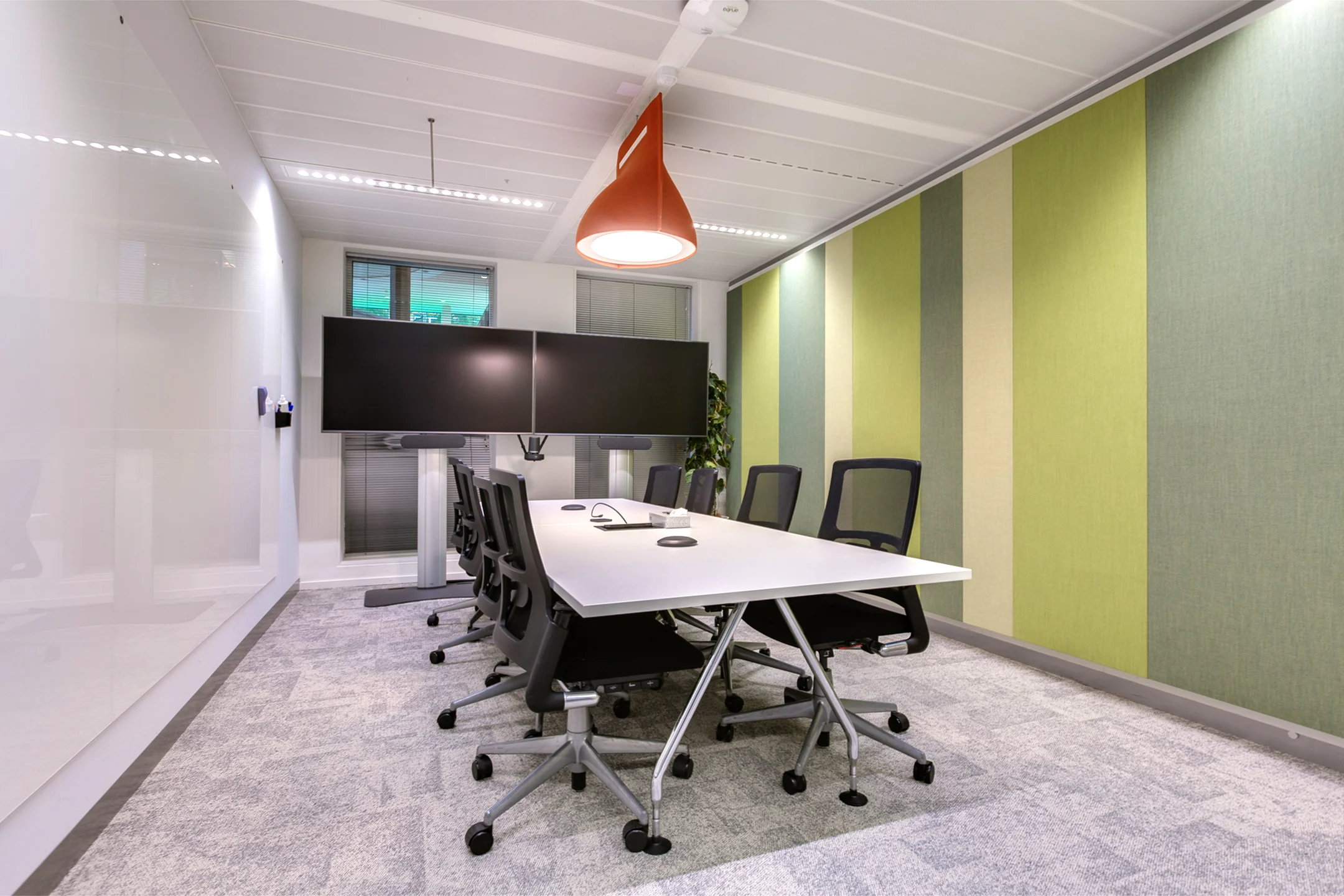 Modern conference room at Carel van Bylandtlaan with a large table, office chairs, dual screens, and striped green wall panels.