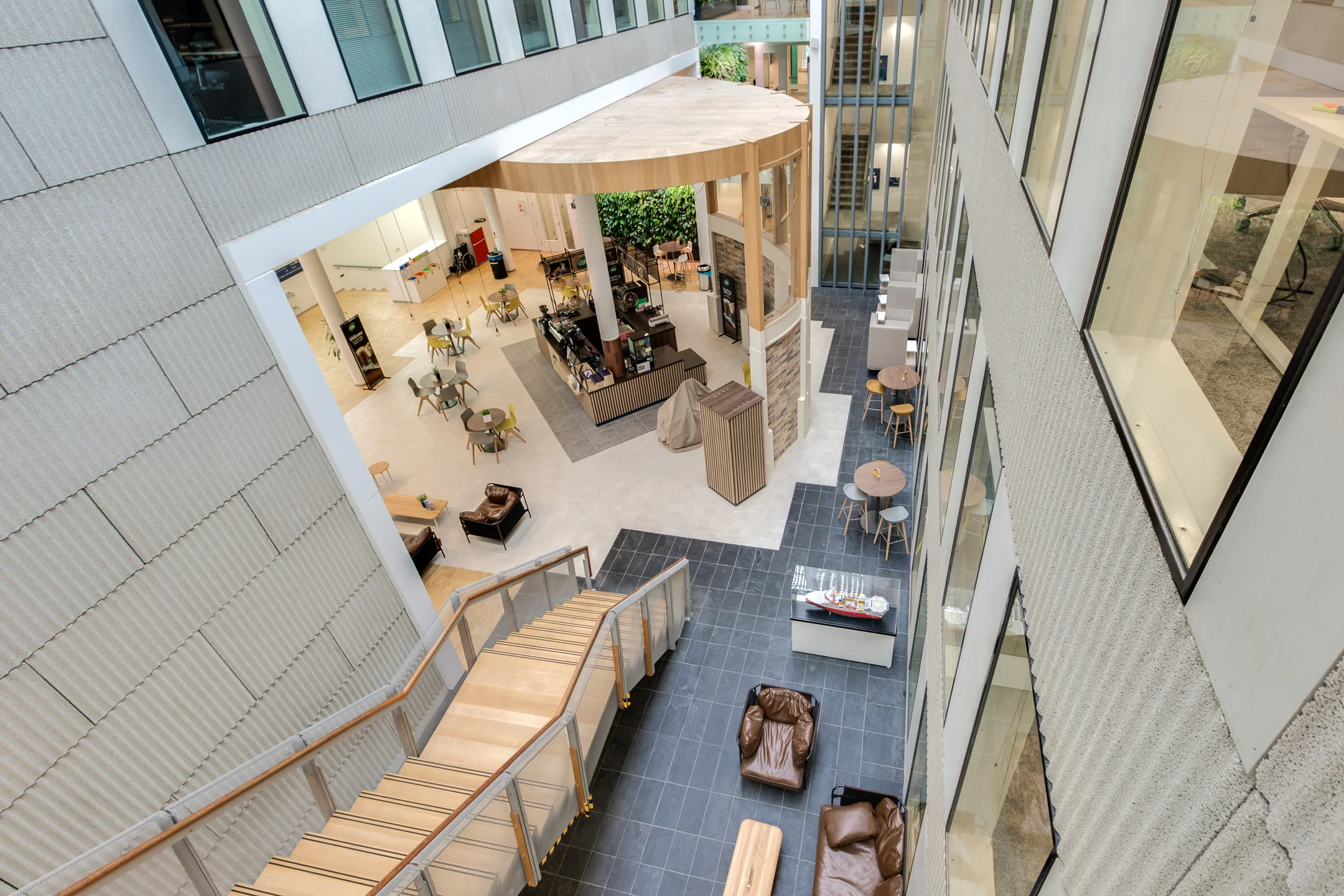 Modern atrium interior of an office building on Carel van Bylandtlaan with seating areas, a coffee bar, and wooden staircase.