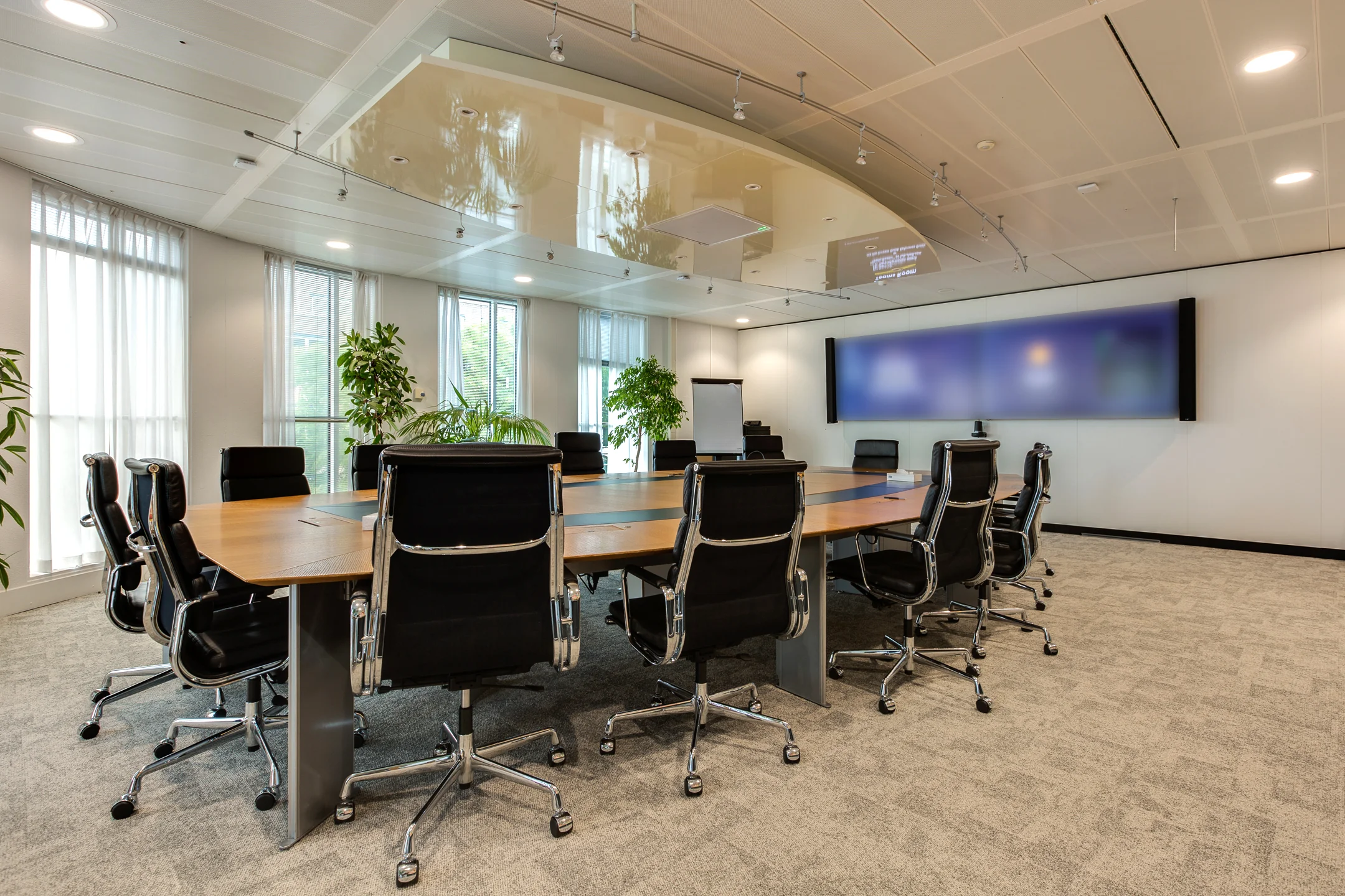 Modern conference room on Carel van Bylandtlaan with a large wooden table, black office chairs, and a wide digital screen.