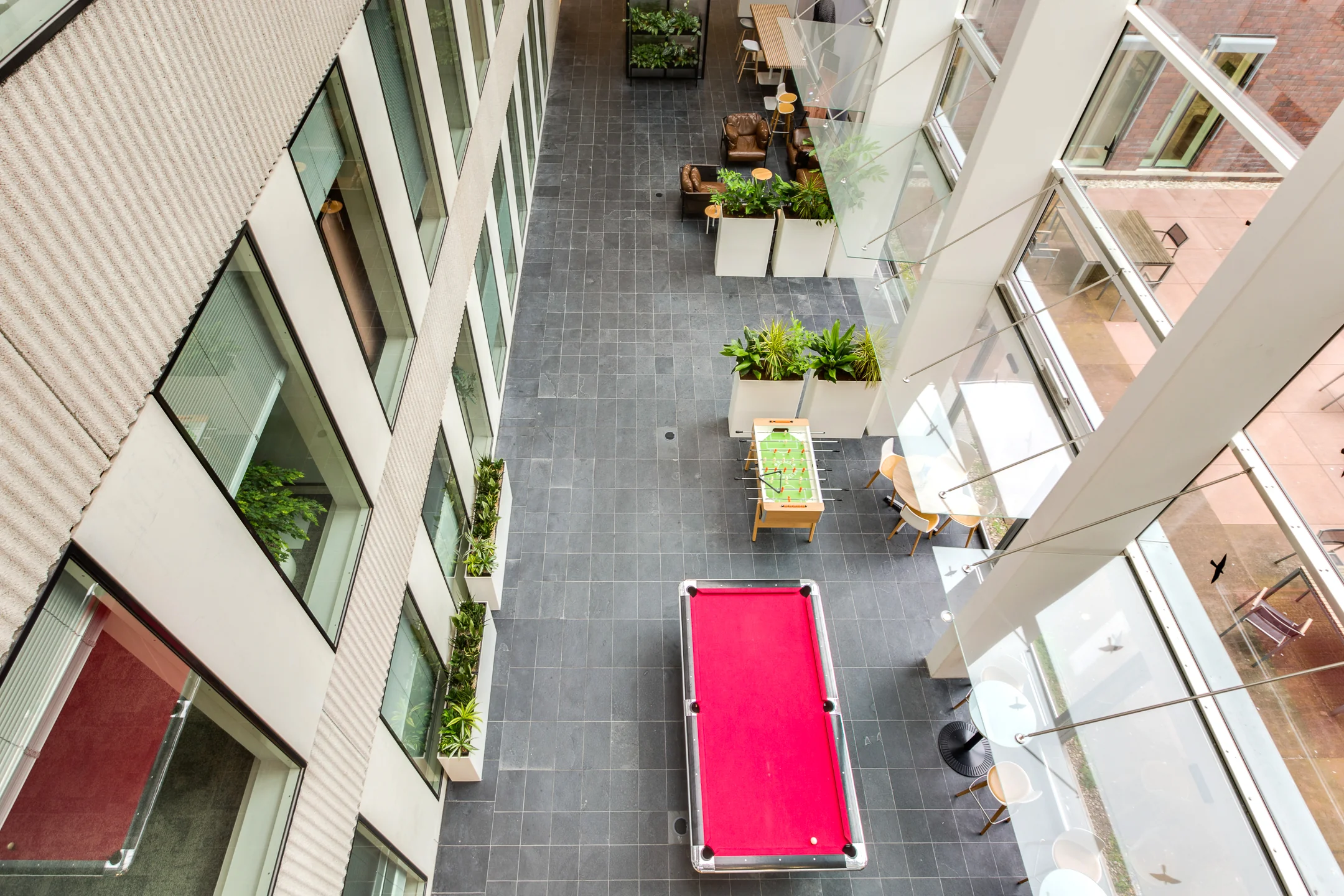 Modern indoor atrium at Carel van Bylandtlaan with a red pool table, foosball table, lounge seating, and large windows.