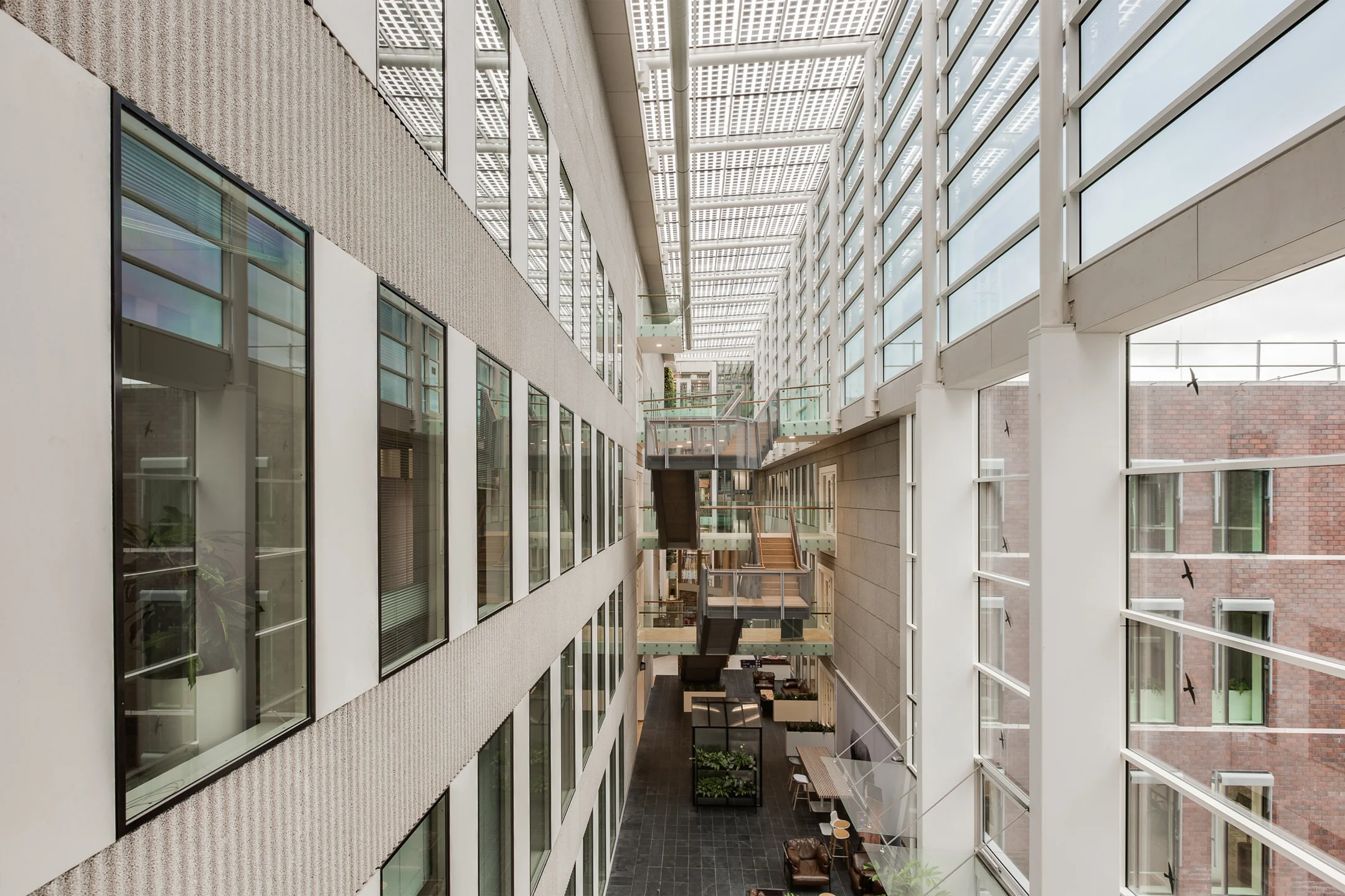 Modern indoor atrium of an office building on Carel van Bylandtlaan with glass walls, skylights, and multiple walkways.