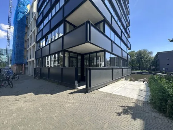 Modern corner building on Willem Parelstraat with reflective windows and a canal-side patio on a sunny day.