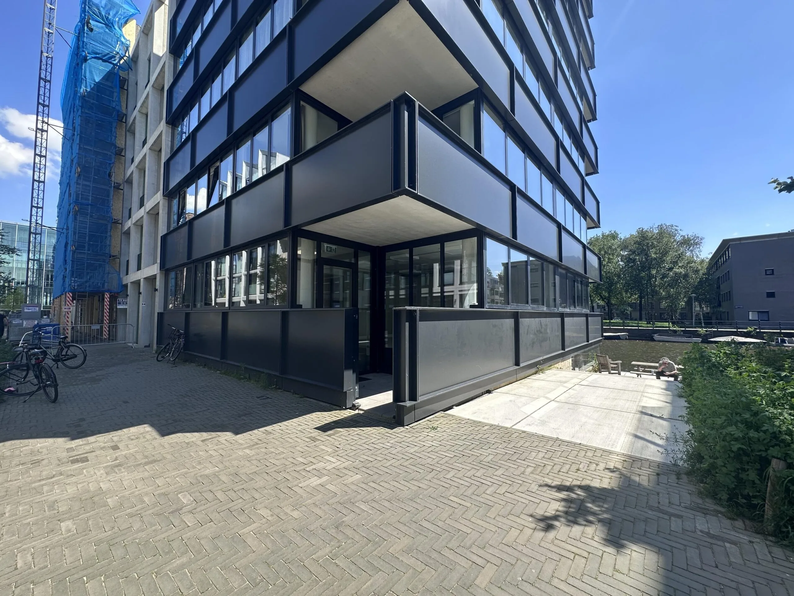 Modern corner building on Willem Parelstraat with reflective windows and a canal-side patio on a sunny day.