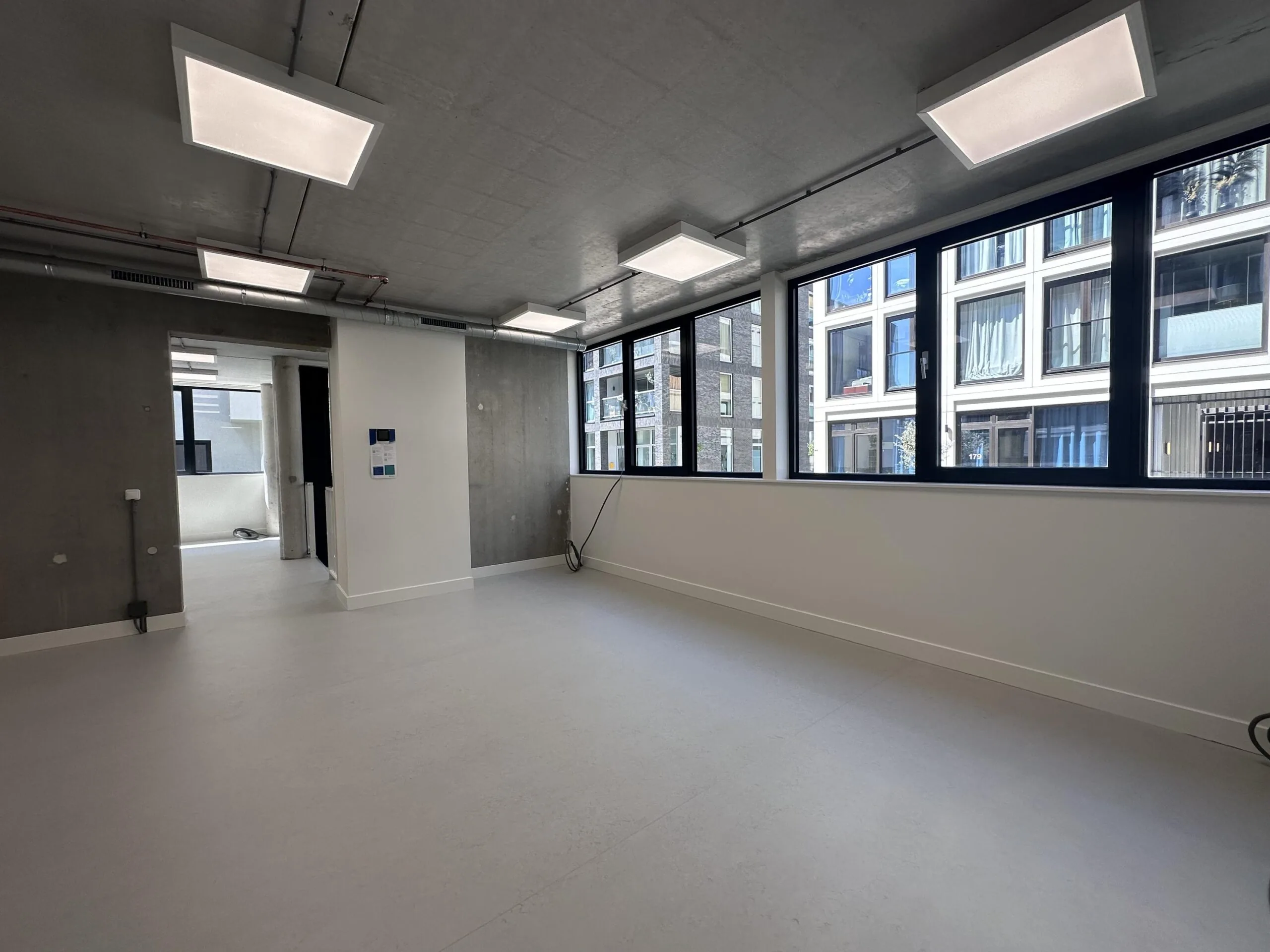 Modern empty office space with large windows on Willem Parelstraat, featuring concrete walls and ceiling lights.