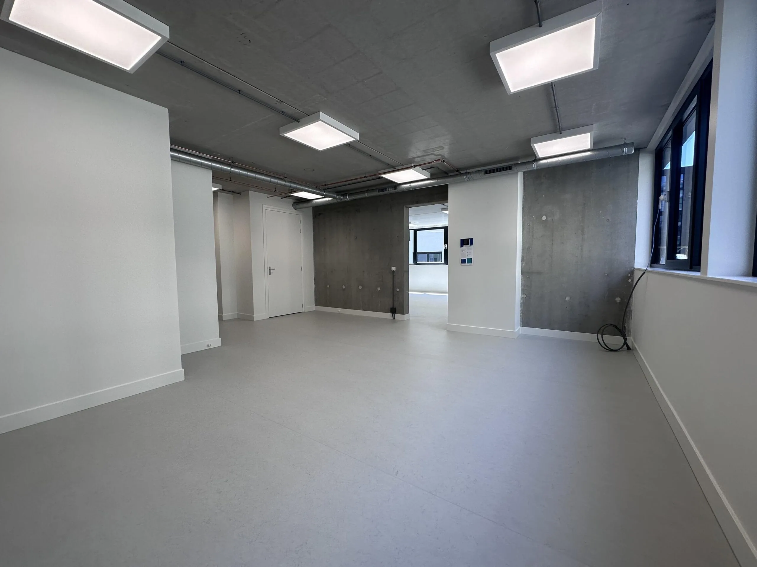 Modern, unfurnished office space on Willem Parelstraat with concrete walls, large windows, and ceiling-mounted LED lighting.