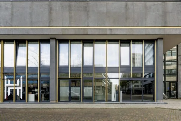 Street-level view of a modern office building facade on James Wattstraat with large reflective windows and golden vertical accents.