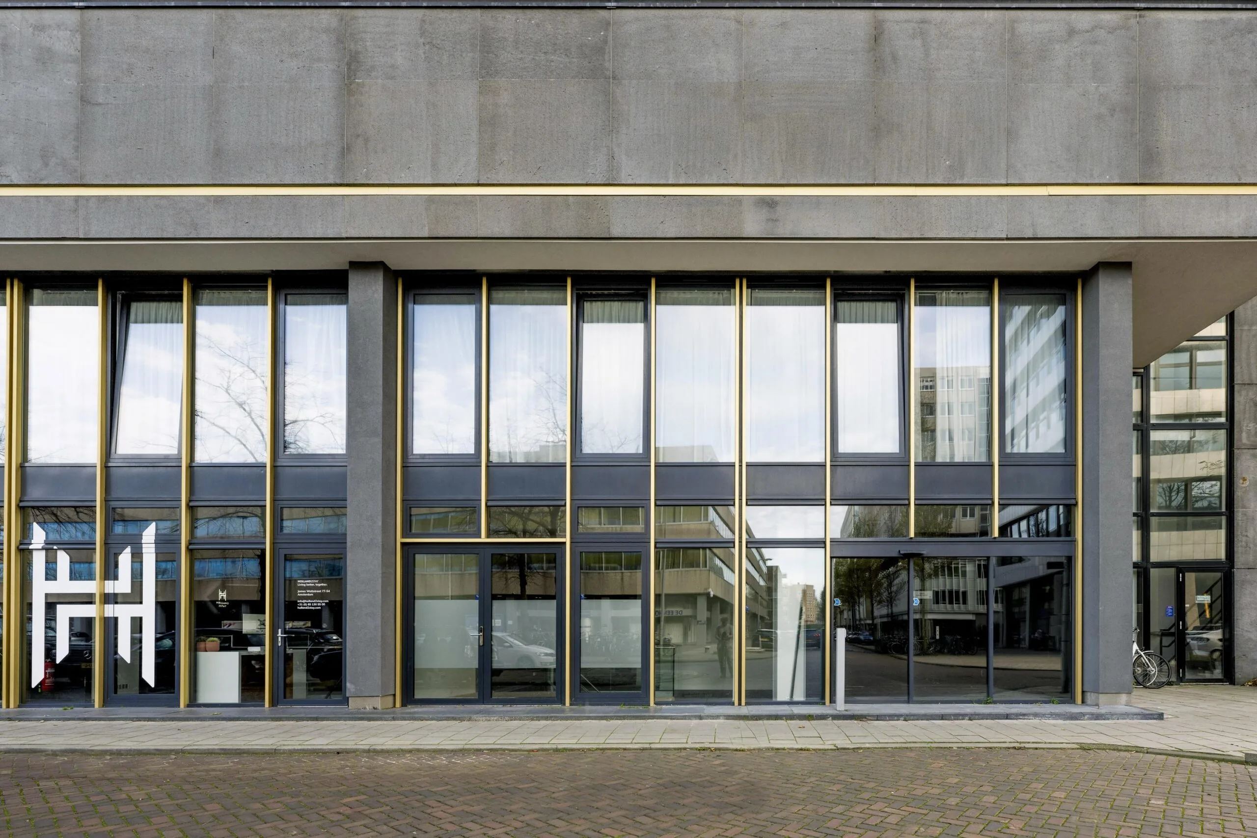 Street-level view of a modern office building facade on James Wattstraat with large reflective windows and golden vertical accents.