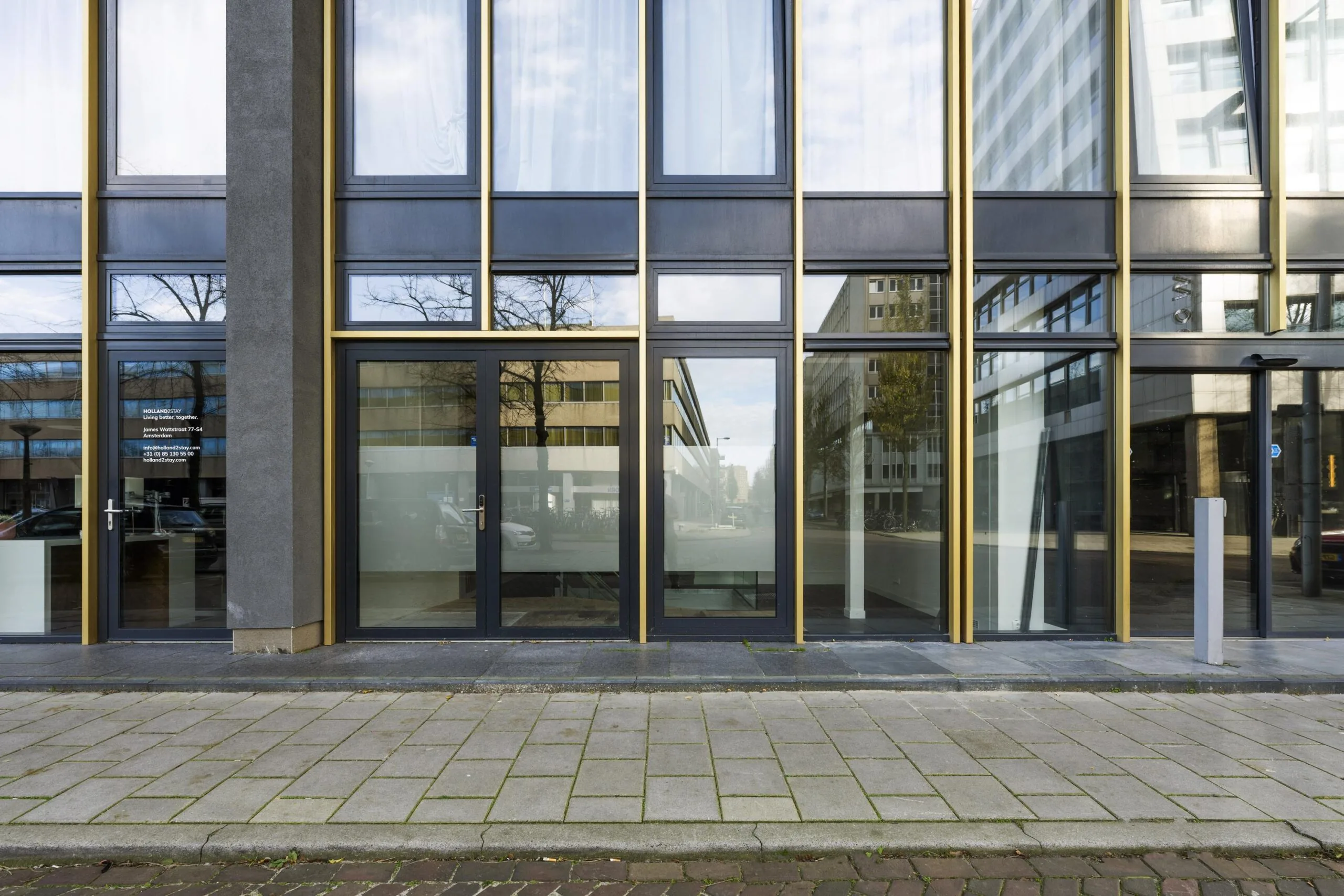 Modern glass office building at James Wattstraat with golden window frames and reflective facade.