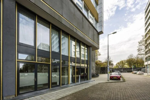 Modern office building on James Wattstraat with large windows and parked cars along the street.