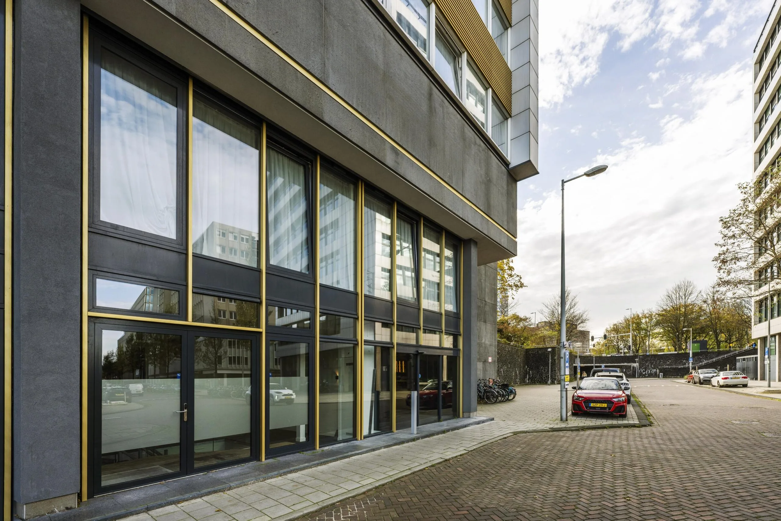 Modern office building on James Wattstraat with large windows and parked cars along the street.