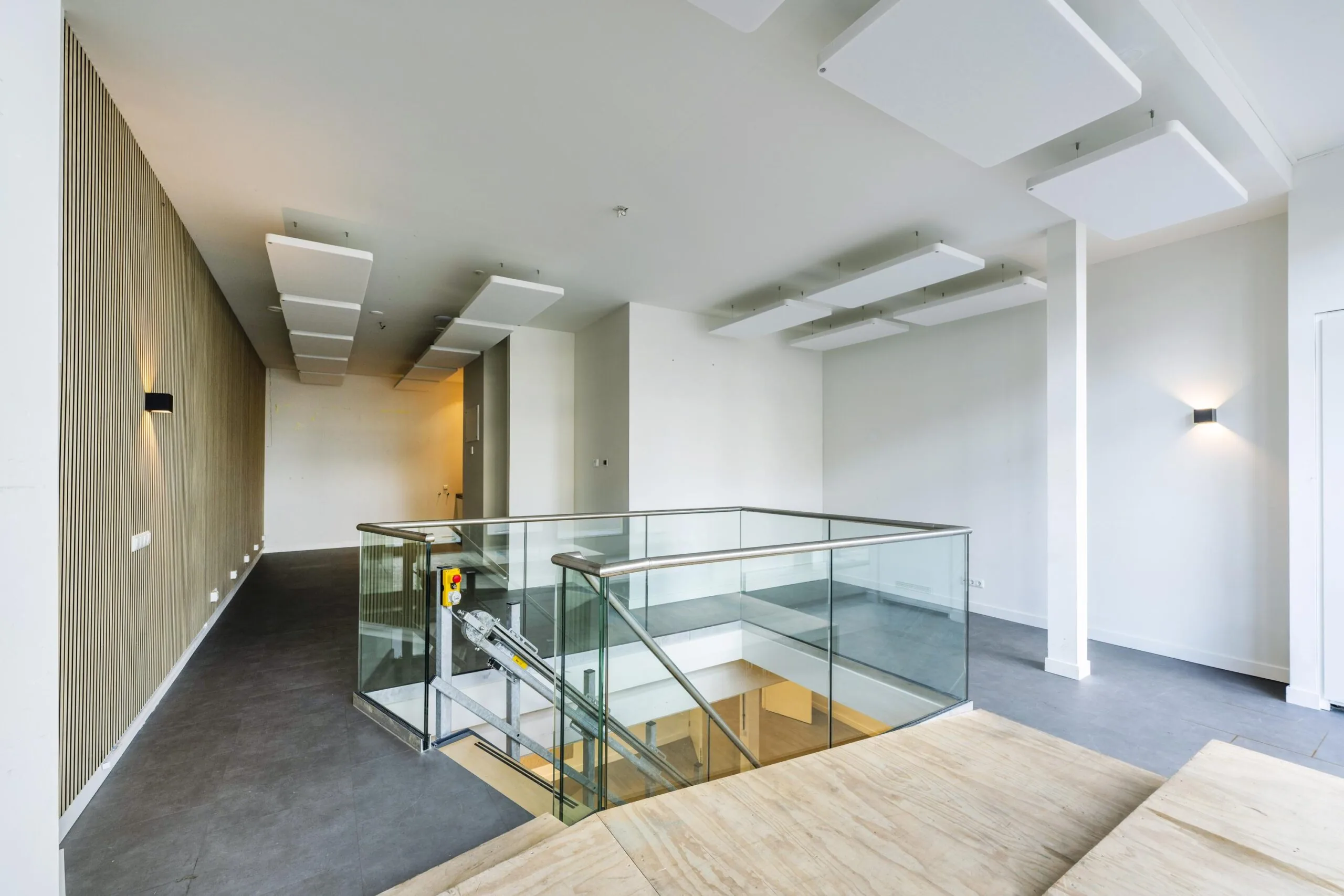 Modern indoor space on James Wattstraat with glass stair railing, acoustic ceiling panels, and wooden wall accents.