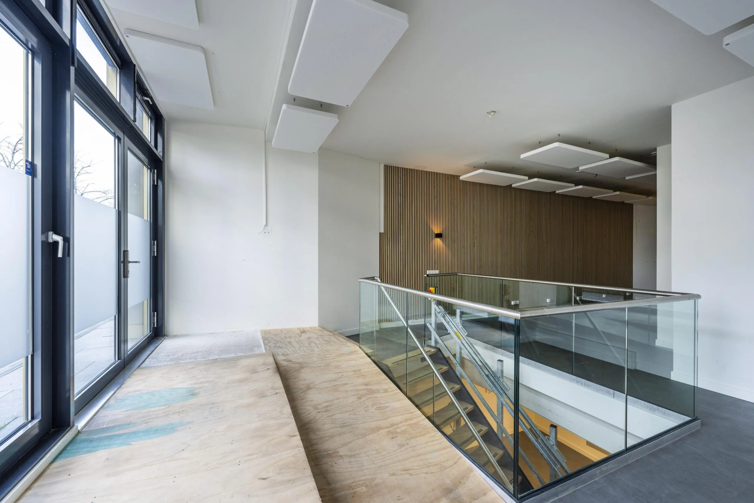 Modern interior of James Wattstraat building featuring a glass staircase, wooden slat wall, and large windows.
