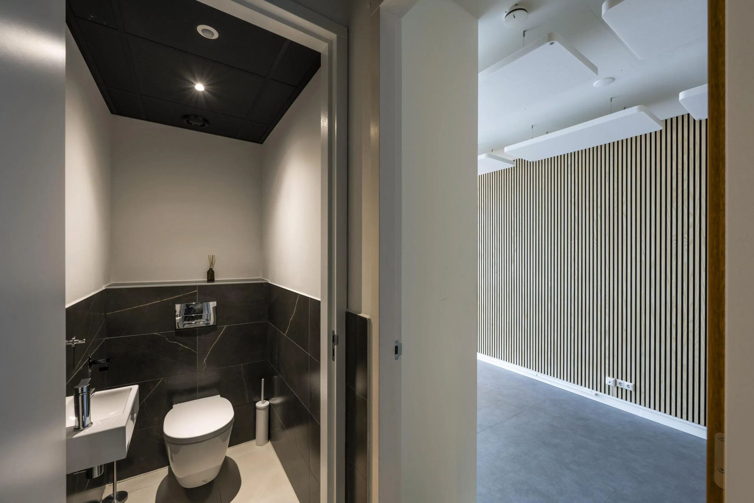 Modern restroom with dark tiled walls and a small sink, located in an office space on James Wattstraat.