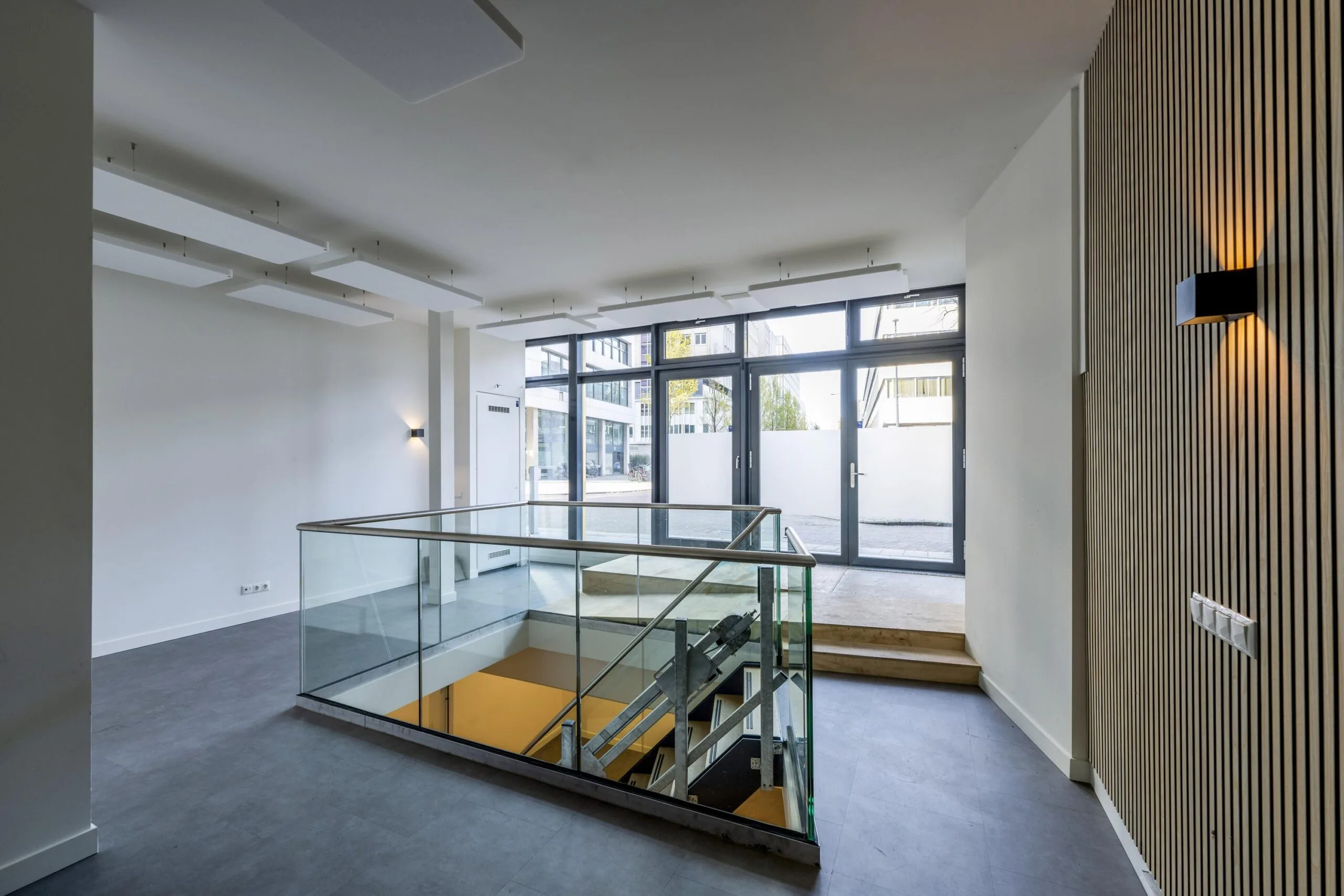 Modern office entrance at James Wattstraat with large windows, glass stairwell, and minimalist interior design.