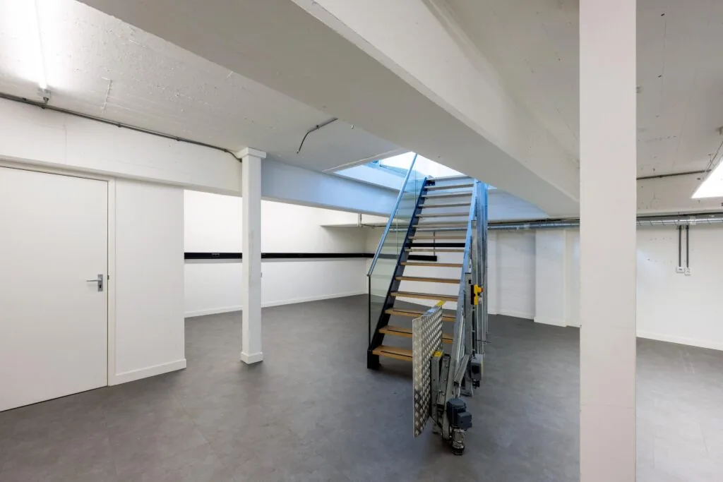 Modern industrial basement interior with a metal staircase and white walls on James Wattstraat.