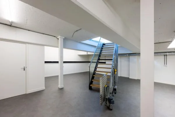 Modern industrial basement interior with a metal staircase and white walls on James Wattstraat.
