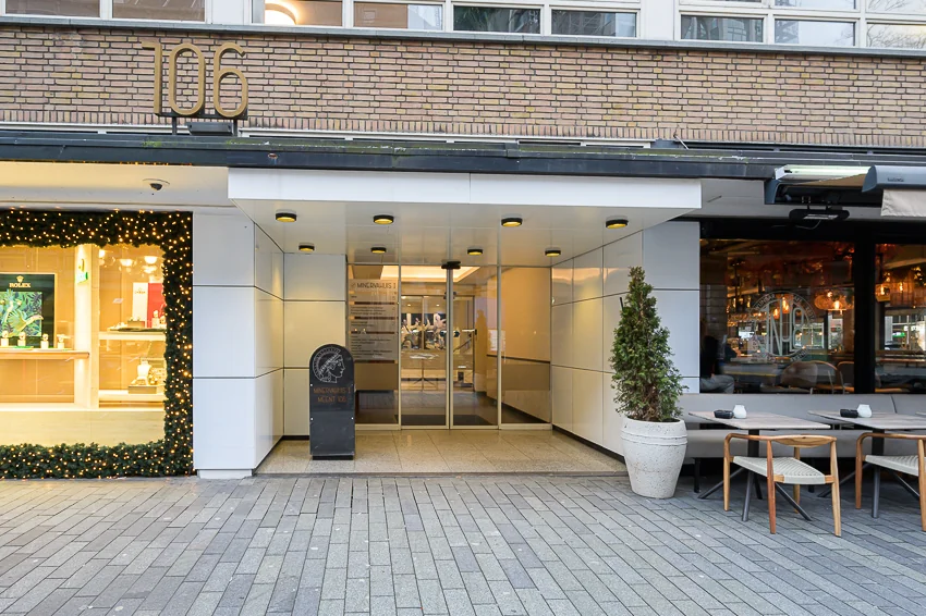 Entree van een modern gebouw op nummer 106 met versierde etalage links en terrasinrichting rechts.