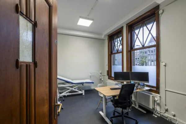 Modern medical consultation room at Westermarkt with a desk, dual monitors, and an examination table.