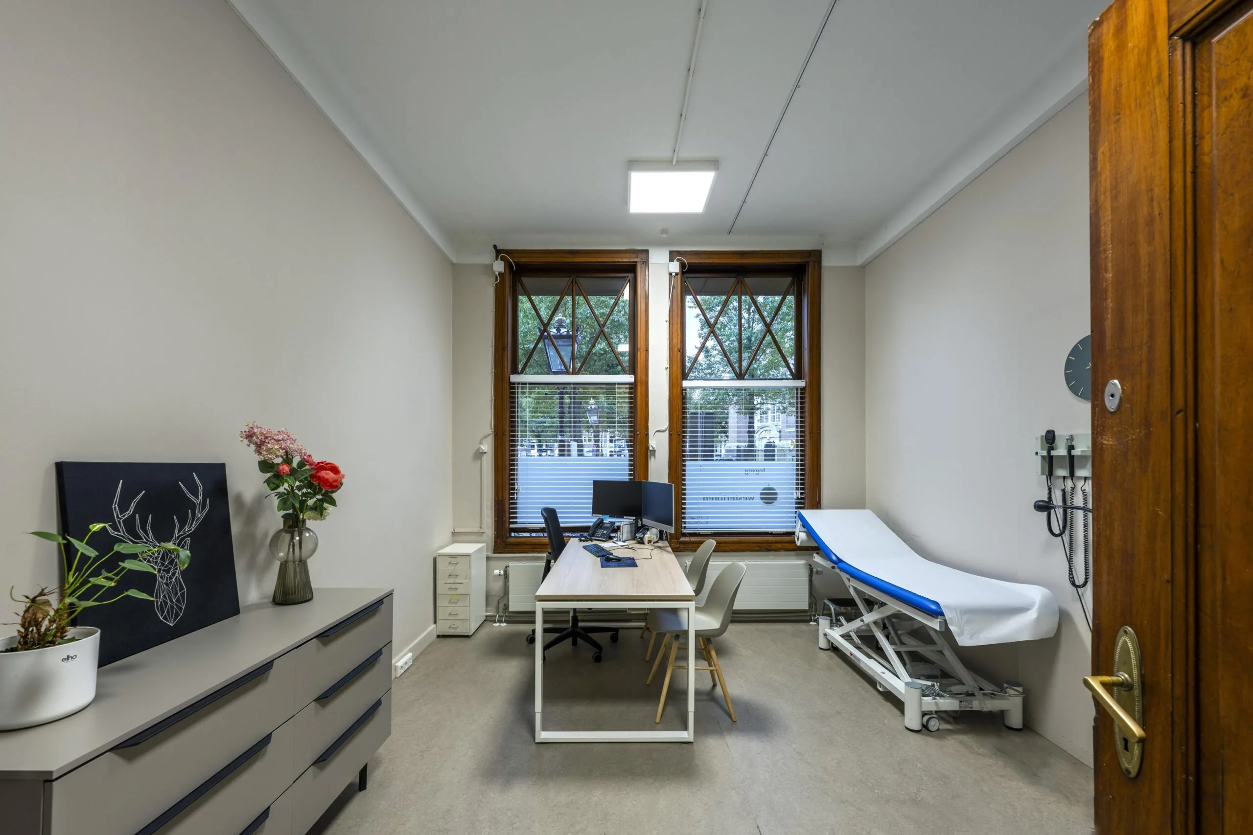 Bright medical consultation room at Westermarkt with a desk, chairs, and examination table.
