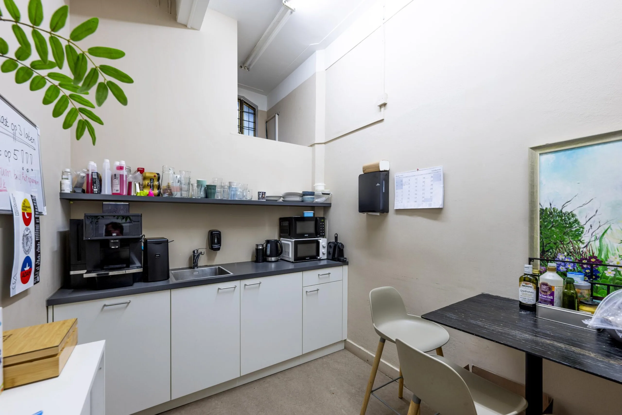 Small office kitchen at Westermarkt with white cabinets, a coffee machine, microwave, and a small dining area.