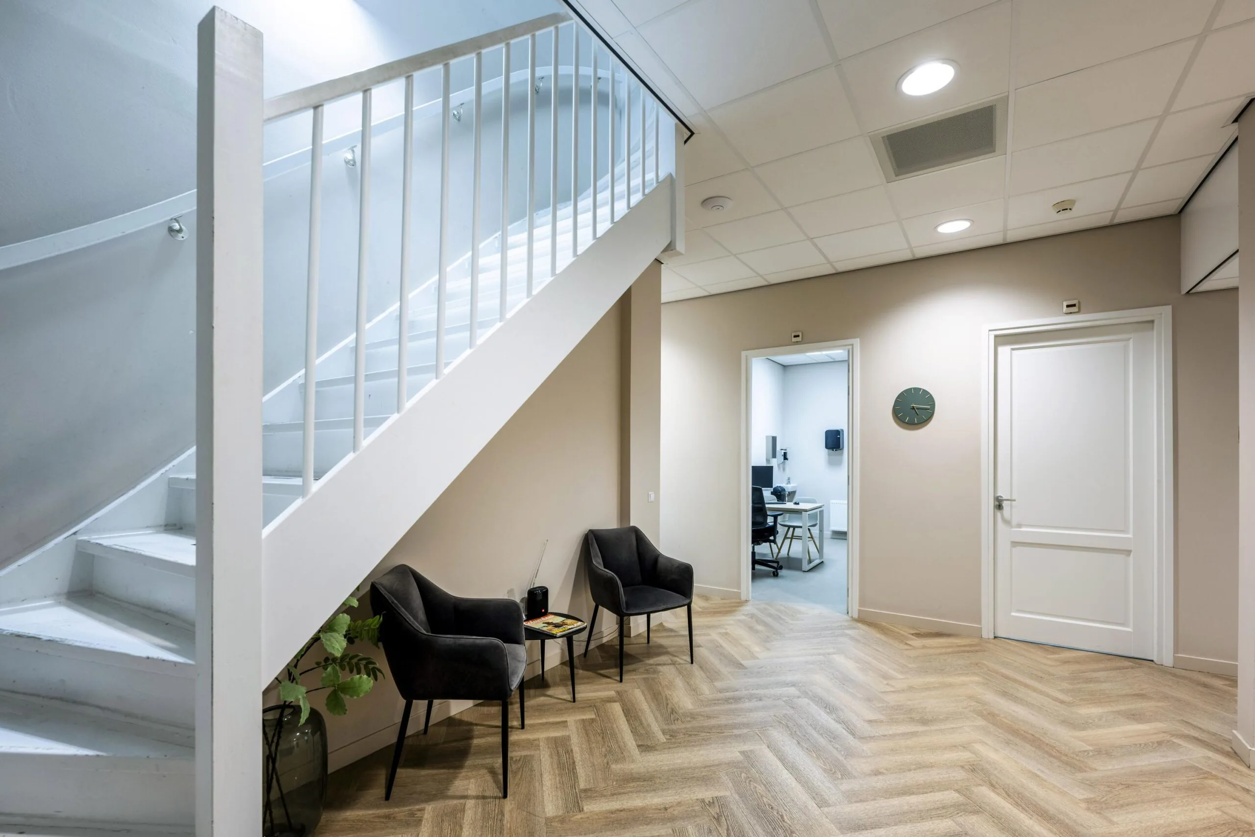 Modern waiting area at Westermarkt with two black chairs, a staircase, and an open door leading to a consultation room.