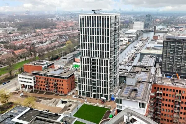 Aerial view of Melkwegstraat featuring a tall modern residential tower surrounded by canals, boats, and urban buildings.