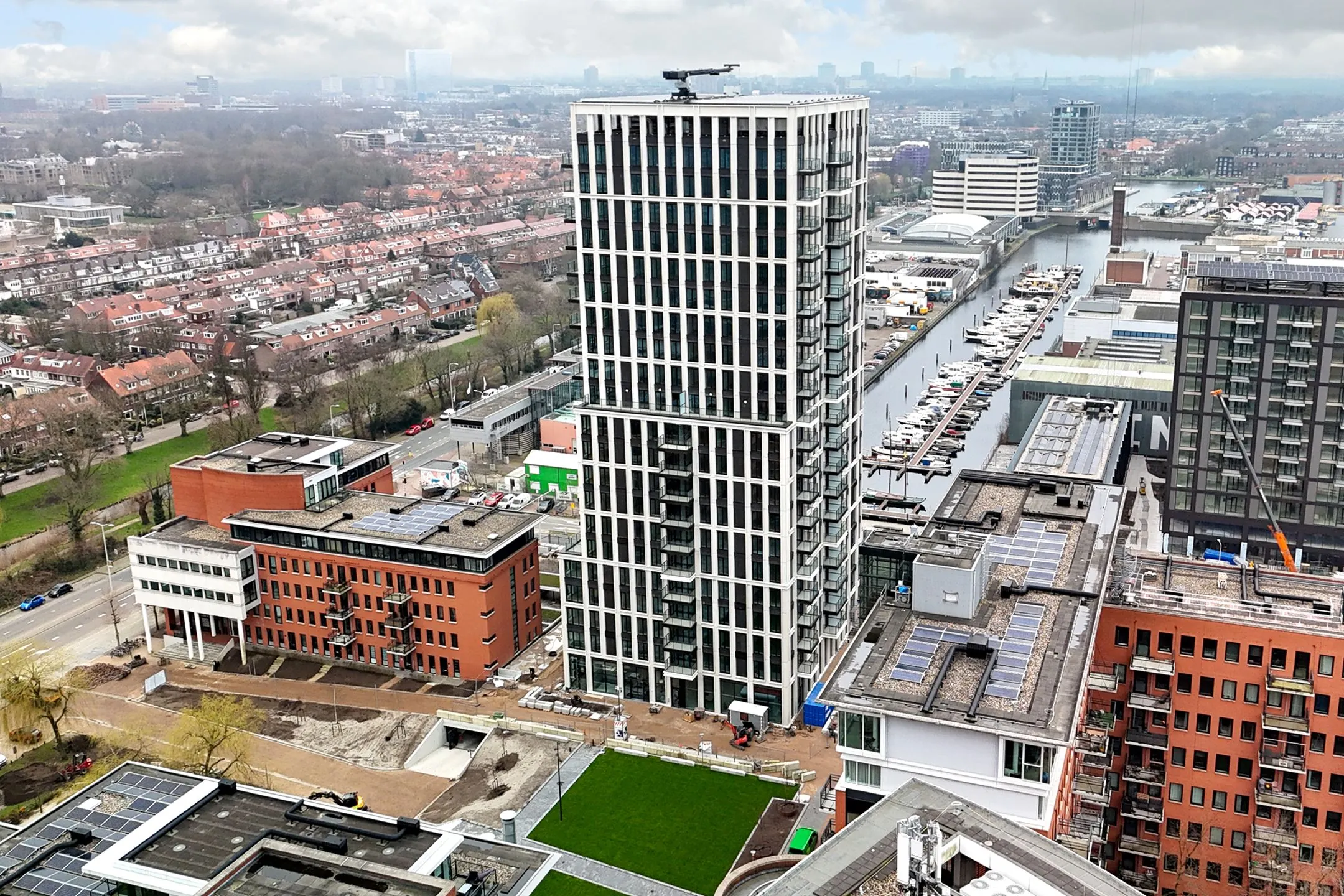 Aerial view of Melkwegstraat featuring a tall modern residential tower surrounded by canals, boats, and urban buildings.