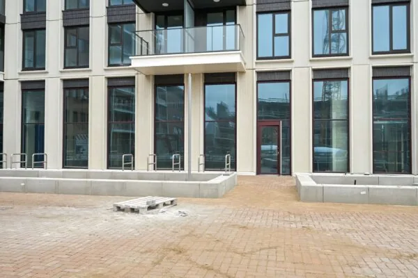 Newly constructed apartment building on Melkwegstraat with large windows, a glass balcony, and an unfinished paved area in front.