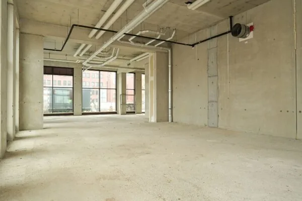 Empty commercial space on Melkwegstraat with exposed concrete walls, large windows, and visible ceiling pipes.