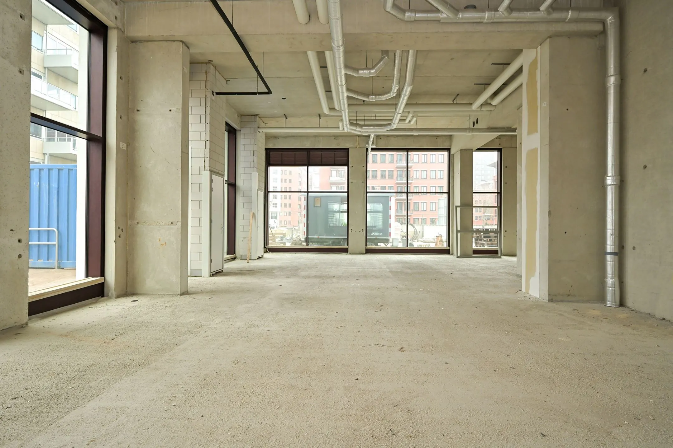 Empty commercial space under construction on Melkwegstraat with large windows and exposed ceiling pipes.
