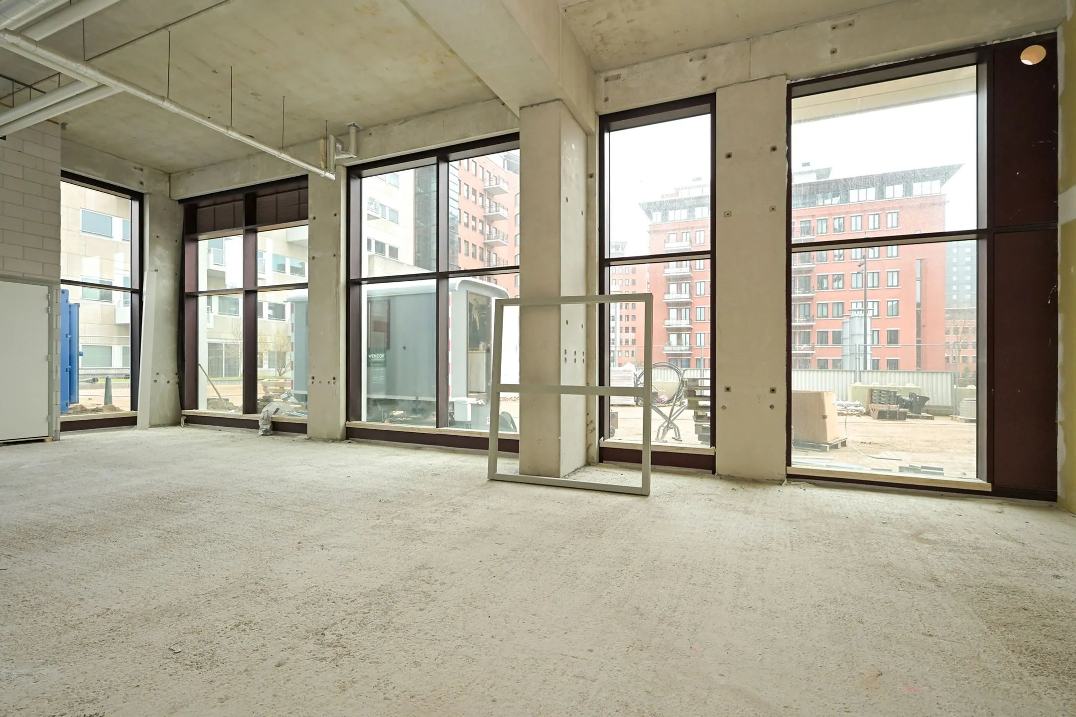 Empty commercial space under construction on Melkwegstraat with large windows overlooking modern apartment buildings.