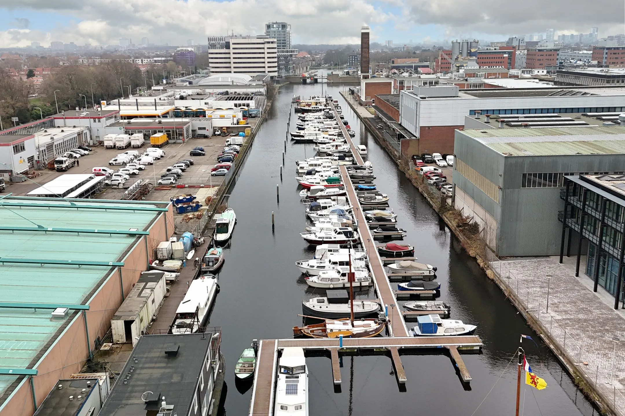 Aerial view of a marina on Melkwegstraat with numerous boats docked along a central pier, surrounded by industrial buildings and parked vehicles.