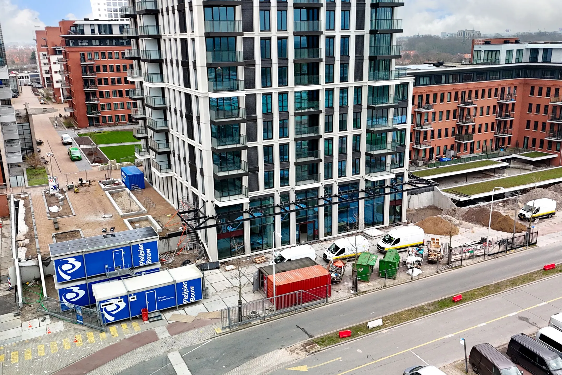 Construction site on Melkwegstraat with modern apartment buildings, containers, and construction vehicles in view.