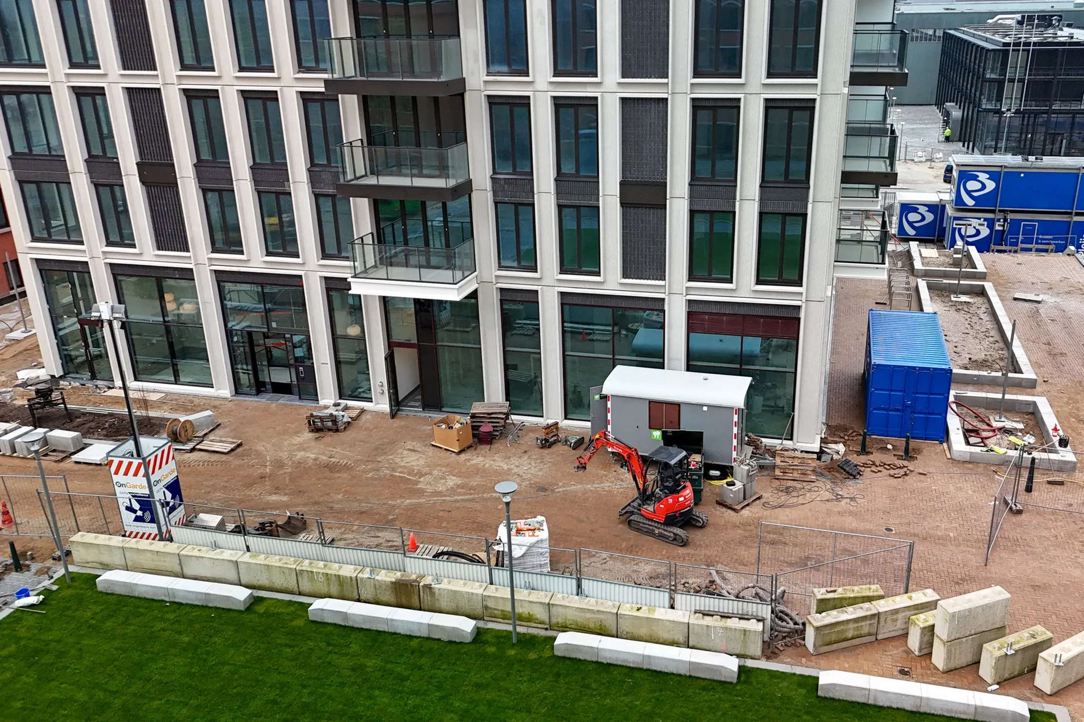 Construction site in front of a modern office or apartment building on Melkwegstraat, with a mini excavator, building materials, and temporary units.