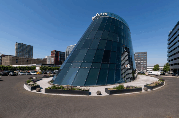 Modern glass building called "The Curve" located on TT Vasumweg in an urban business district.