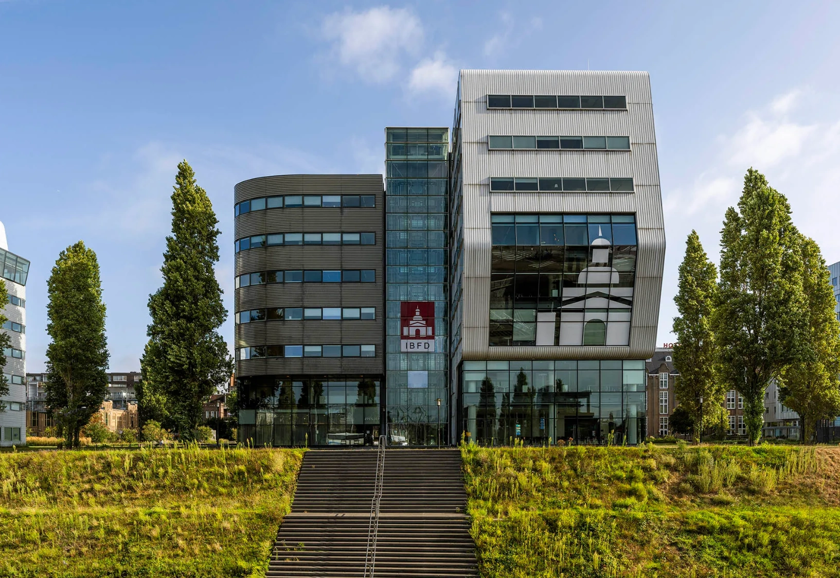 Modern office building of the IBFD at Rietlandpark in Amsterdam, viewed from the front with wide steps and trees in the foreground.