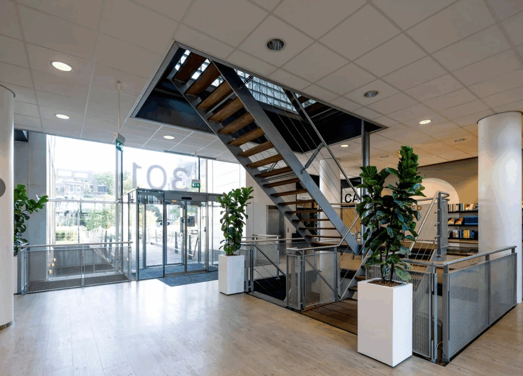 Modern office entrance at Rietlandpark 301 featuring a wooden staircase, glass doors, and indoor plants.