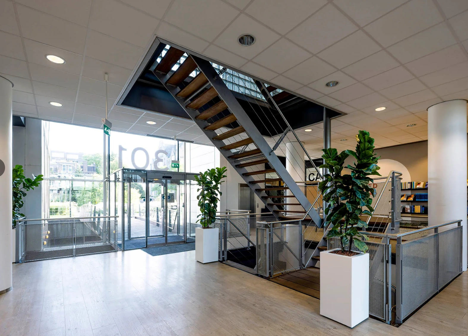 Modern office entrance at Rietlandpark 301 featuring a wooden staircase, glass doors, and indoor plants.