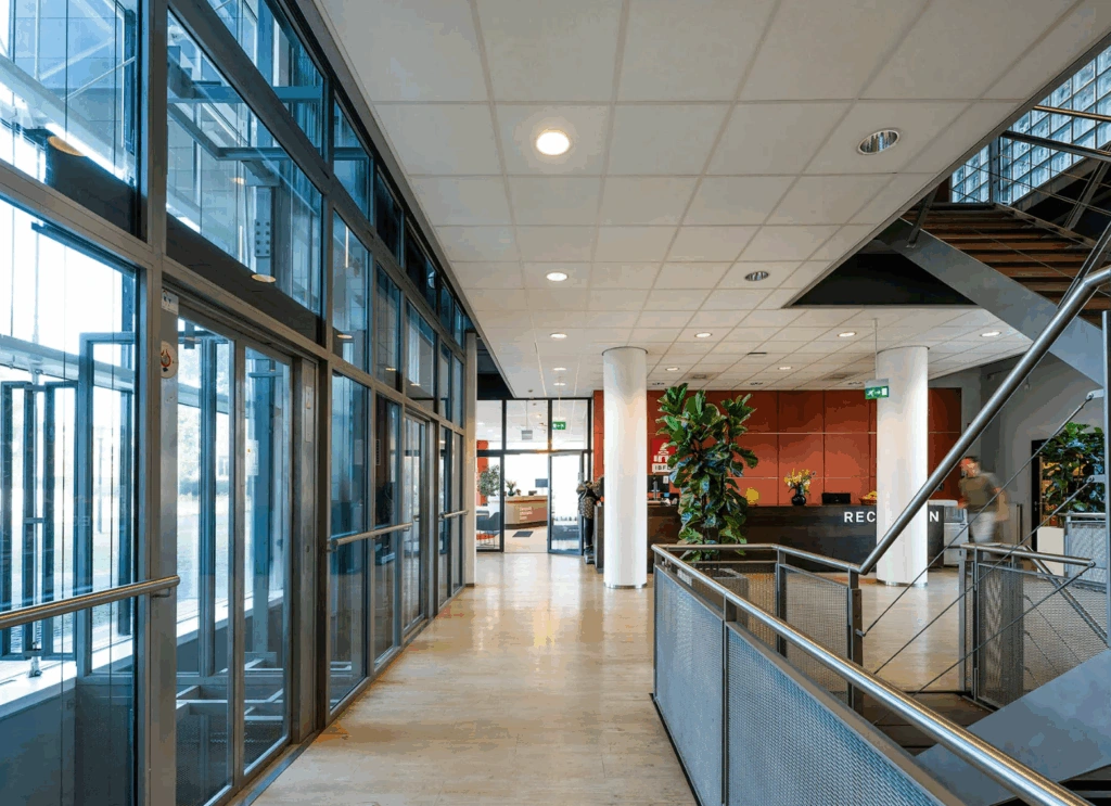 Modern reception area of the Rietlandpark building with glass walls, indoor plants, and a staircase.
