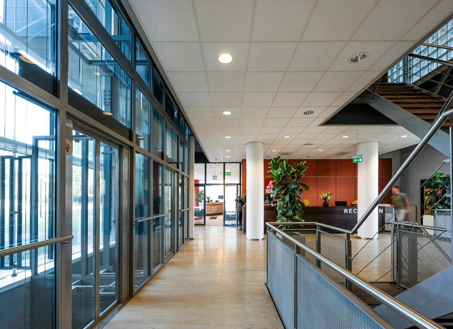 Modern reception area of the Rietlandpark building with glass walls, indoor plants, and a staircase.