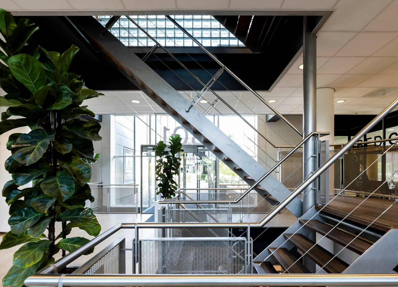 Modern interior of Rietlandpark with metal staircases, large glass windows, and indoor plants.